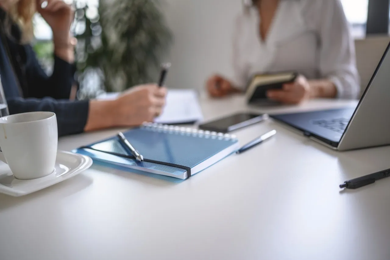 Two professionals in a strategy session at a bright table with notebooks, a tablet, and a laptop